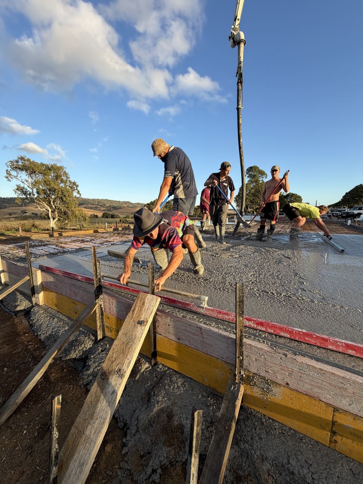 Crew finishing a rural property slab pour at sunset