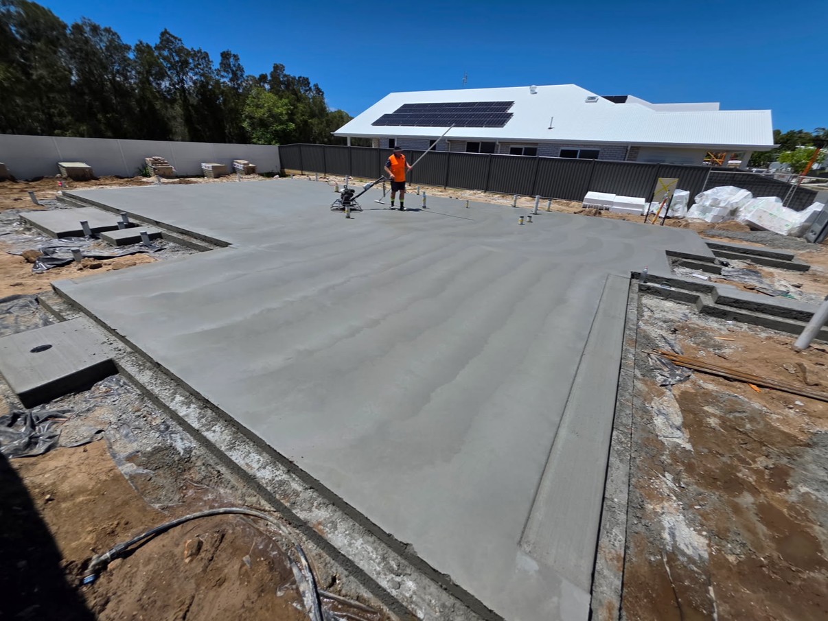 House slab pour being screeded with power float, solar-panelled home behind
